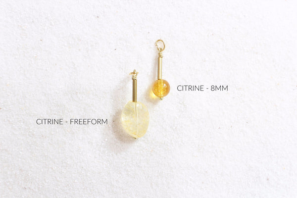 citrine pendants with gold brass detail laid out on white sand