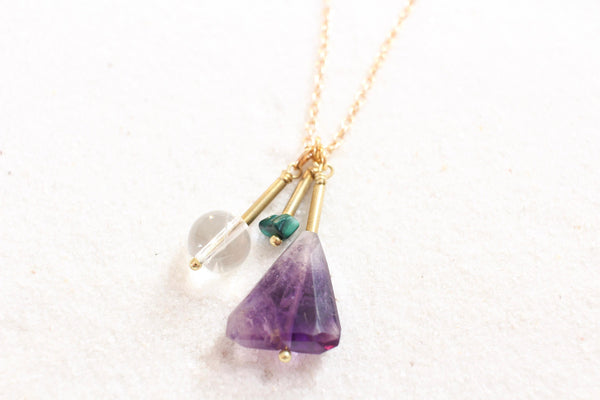 large amethyst pendant, malachite pendant and clear quartz pendant on a thin gold chain, laying on white sand