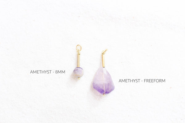 8mm and freeform amethyst pendants with gold detail, laying on white sand