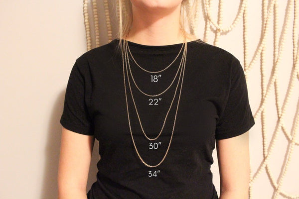 neutral beaded background, thin caucasian woman wearing various necklace lengths to show different sizes. wearing black shirt. 18", 22", 30" 34" shown