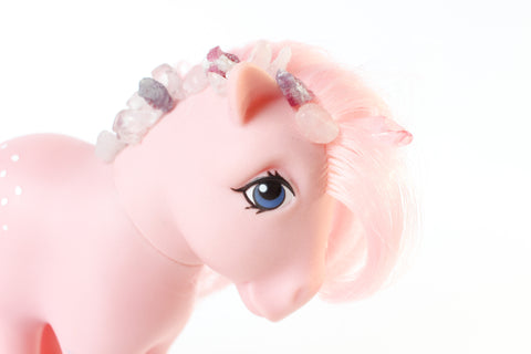 light pink my little pony figurine with a pink quartz unicorn horn, and pink tourmaline, rose quartz and kunzite gems running down the side of her mane. close up view of her face from the side. white background.