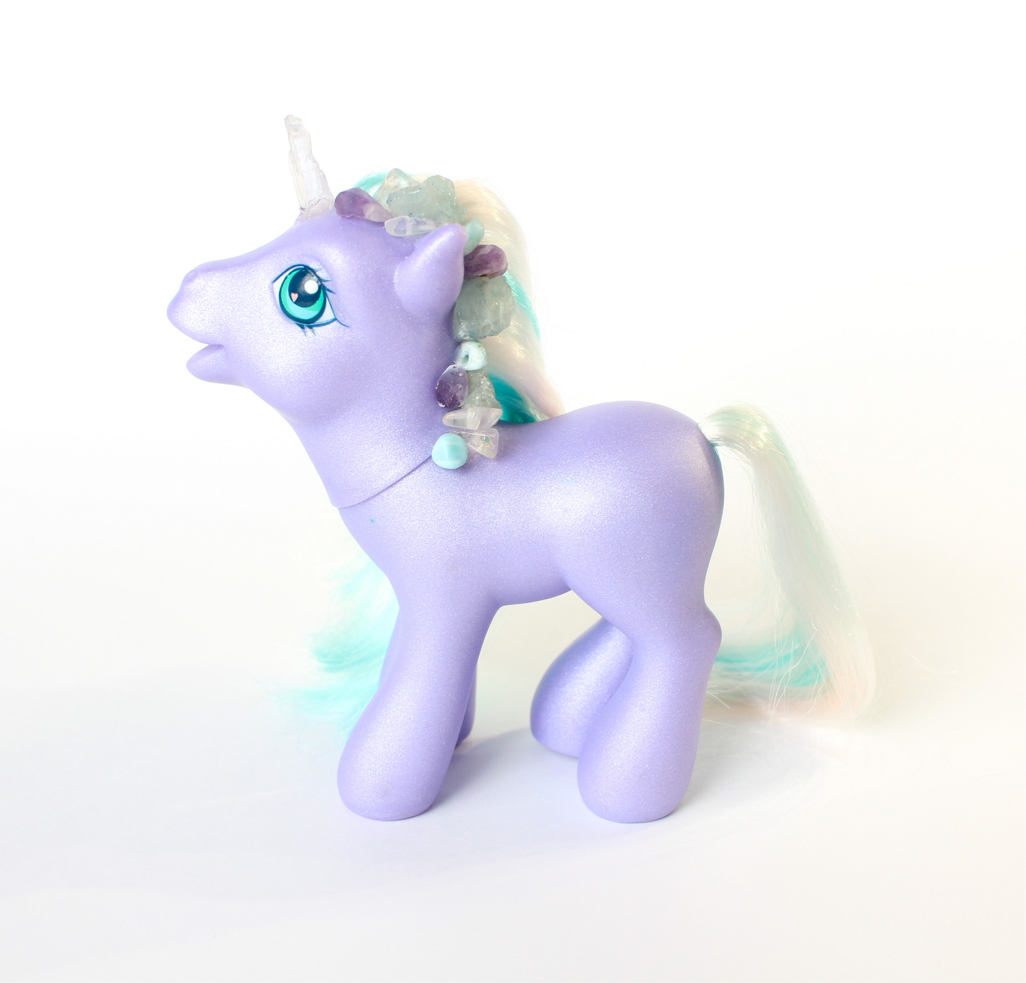 shimmery purple My Little Pony figurine with white and teal hair. side profile. pony has been altered and has had a quartz horn attached, and multiple blue, clear and purple crystals along the main. white background.