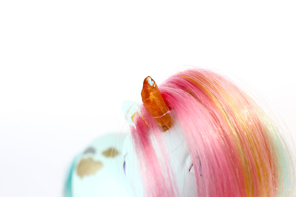 mint blue my little pony figurine with a rainbow coloured mane, an orange crystal horn and crystals trailing down her mane. white background, close up on horn