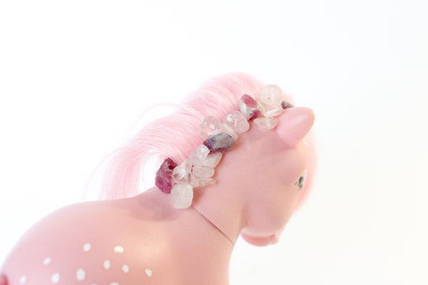 light pink my little pony figurine with a pink quartz unicorn horn, and pink tourmaline, rose quartz and kunzite gems running down the side of her mane. rear 45 degree angle view, showcasing the gemstones running down her neck. white background.