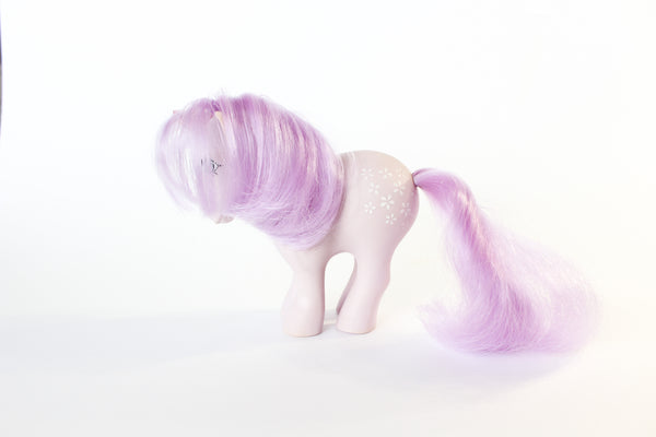 light purple my little pony figure with a pink quartz point for a unicorn horn, and pink and purple gemstones running down her mane. the gemstones have pink glitter between them. side  view, showing her perfectly cared for mane.. white background