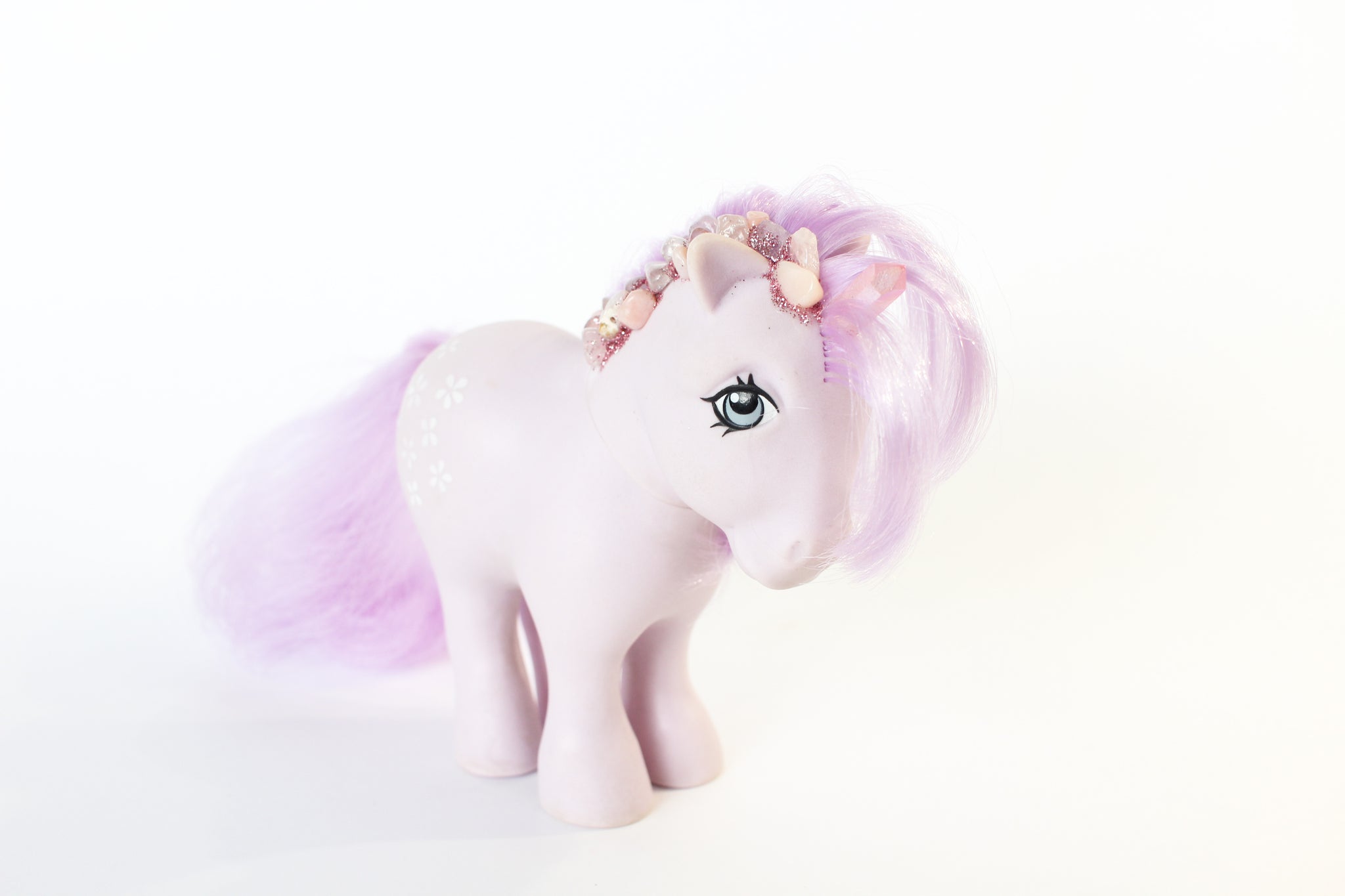 light purple my little pony figure with a pink quartz point for a unicorn horn, and pink and purple gemstones running down her mane. the gemstones have pink glitter between them. front 45degree angle view. white background