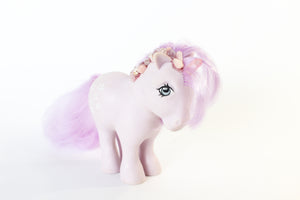 light purple my little pony figure with a pink quartz point for a unicorn horn, and pink and purple gemstones running down her mane. the gemstones have pink glitter between them. front 45degree angle view. white background