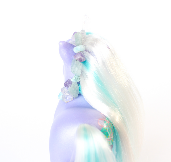 shimmery purple My Little Pony figurine with white and teal hair. rear view. pony has been altered and has had a quartz horn attached, and multiple blue, clear and purple crystals along the main. white background.