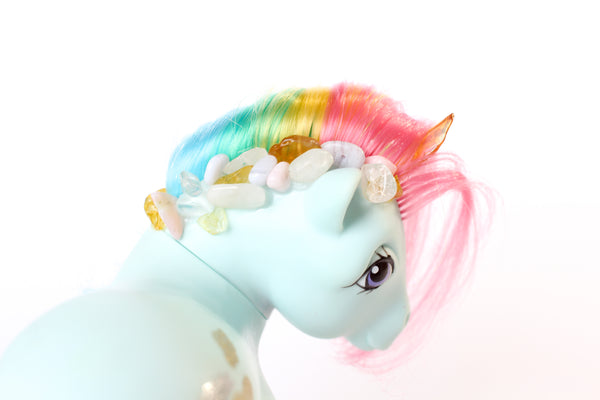 mint blue my little pony figurine with a rainbow coloured mane, an orange crystal horn and crystals trailing down her mane. white background, view from back