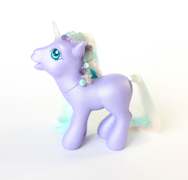 shimmery purple My Little Pony figurine with white and teal hair. side profile. pony has been altered and has had a quartz horn attached, and multiple blue, clear and purple crystals along the main. white background.