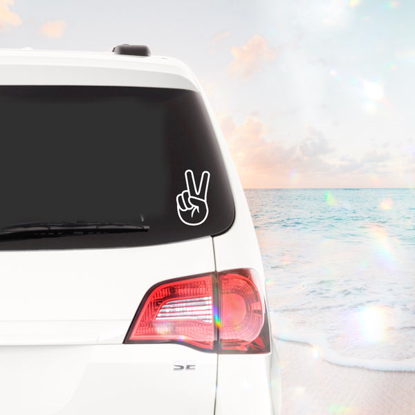 rear view of a white SUV in front of a beach with the very beginning of a sunset. on the rear window of the SUV is the peace sign decal, bottom right corner